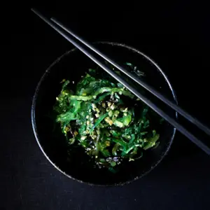 მიმზიდველი მწვანე წყალმცენარეების სალათით სავსე შავი ჯამი